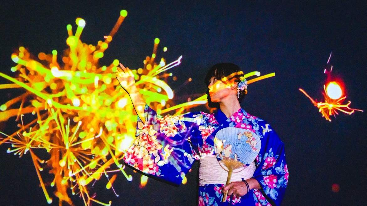花火の光に包まれる浴衣の女性